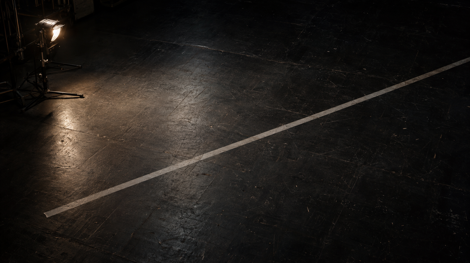 A single strip of marking tape forming a diagonal line across an empty, dark stage floor, unoccupied